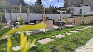 Ein Terrassenbereich im Freien mit Tischen und Stühlen, umgeben von viel Grün und einer Steinmauer.