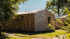 Una cabaña moderna de madera con techo inclinado, un ventanal pequeño y una puerta.