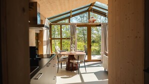 Un interior moderno con techo de madera, ventanas amplias, zona de comedor con mesa y sillas redondas, y un sofá.