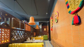 A restaurant with yellow booths, orange hanging lamps, and decorative wall hangings. - Srimad Hotel (Ujjain)
