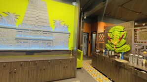A hotel lobby with a bright yellow wall, a large decorative wall piece, and a green statue. - Srimad Hotel (Ujjain)