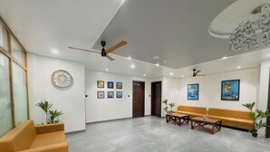 A spacious lobby with a marble floor, a wooden bench, a sofa, and ceiling fans. - Srimad Hotel (Ujjain)