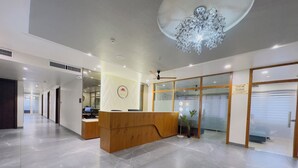 A modern reception area with a wooden reception desk, a large chandelier, and a glass door leading to a parking garage. - Srimad Hotel (Ujjain)
