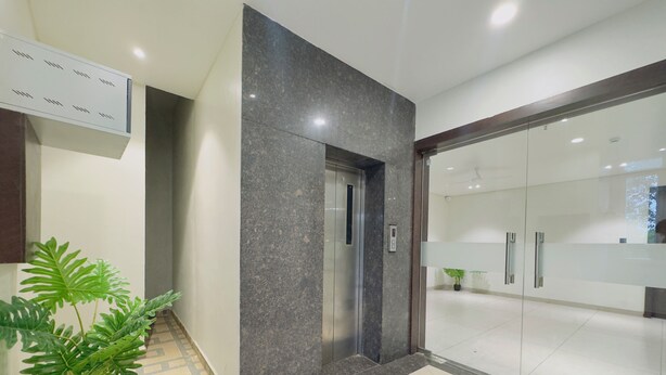 A modern lobby with a marble floor, a potted plant, a reception desk, and a glass elevator. - Srimad Hotel (Ujjain)
