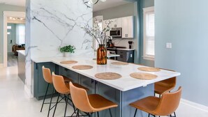 Una cocina moderna con una isla de mármol, cuatro taburetes de bar y un jarrón central con flores.