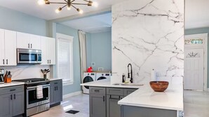 Una cocina moderna con gabinetes grises, un horno de acero inoxidable, un microondas y un lavamanos con una salpicadura de mármol.
