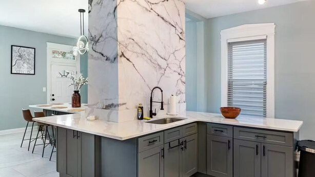Una cocina moderna con una isla grande, armarios grises y una pared de acento de mármol.