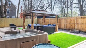 Un jardín trasero con un jacuzzi, un porche cubierto y mobiliario exterior.
