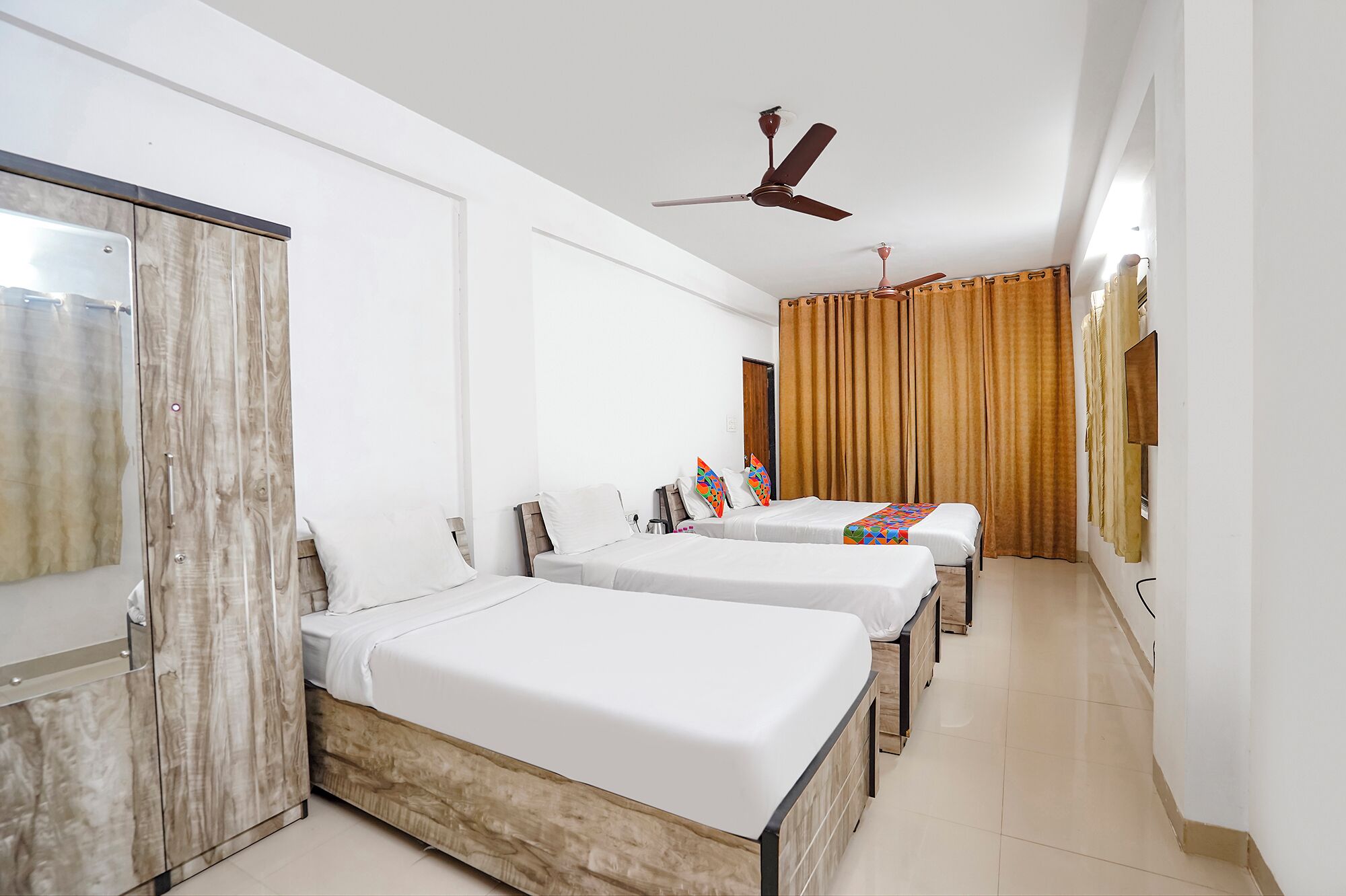 Habitación de hotel con tres camas individuales, un armario, ventilador de techo y baño con cortina de ducha.