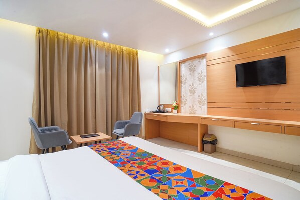 Une chambre d’hôtel avec un lit, deux chaises, un bureau, une télévision et un tapis à motifs.