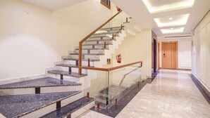 Un intérieur moderne avec un escalier en marbre, des rampes en verre et des spots encastrés au plafond.