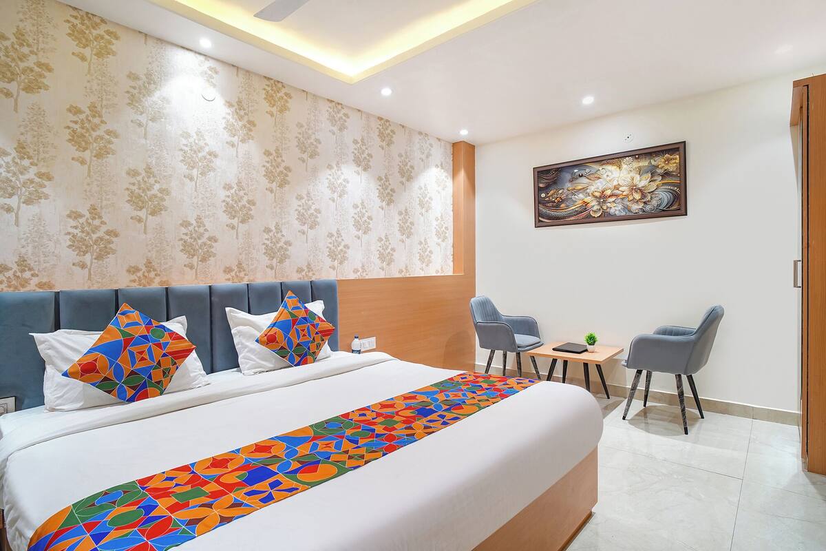 Una habitación de hotel con una cama grande, dos sillas, una mesita y un cuadro en la pared.
