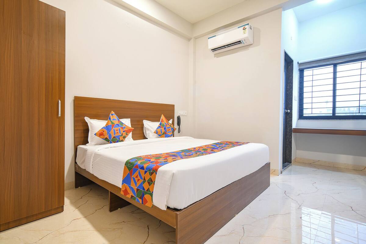 Una cama bien tendida con una colcha de estampado geométrico, un cabecero de madera y un aire acondicionado de pared.