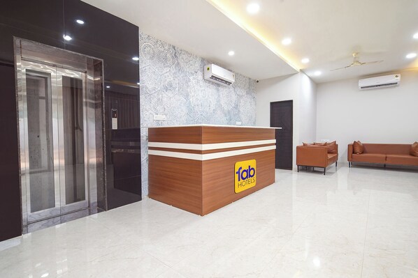 A hotel reception area with a wooden reception desk, a digital clock, and two air conditioning units.