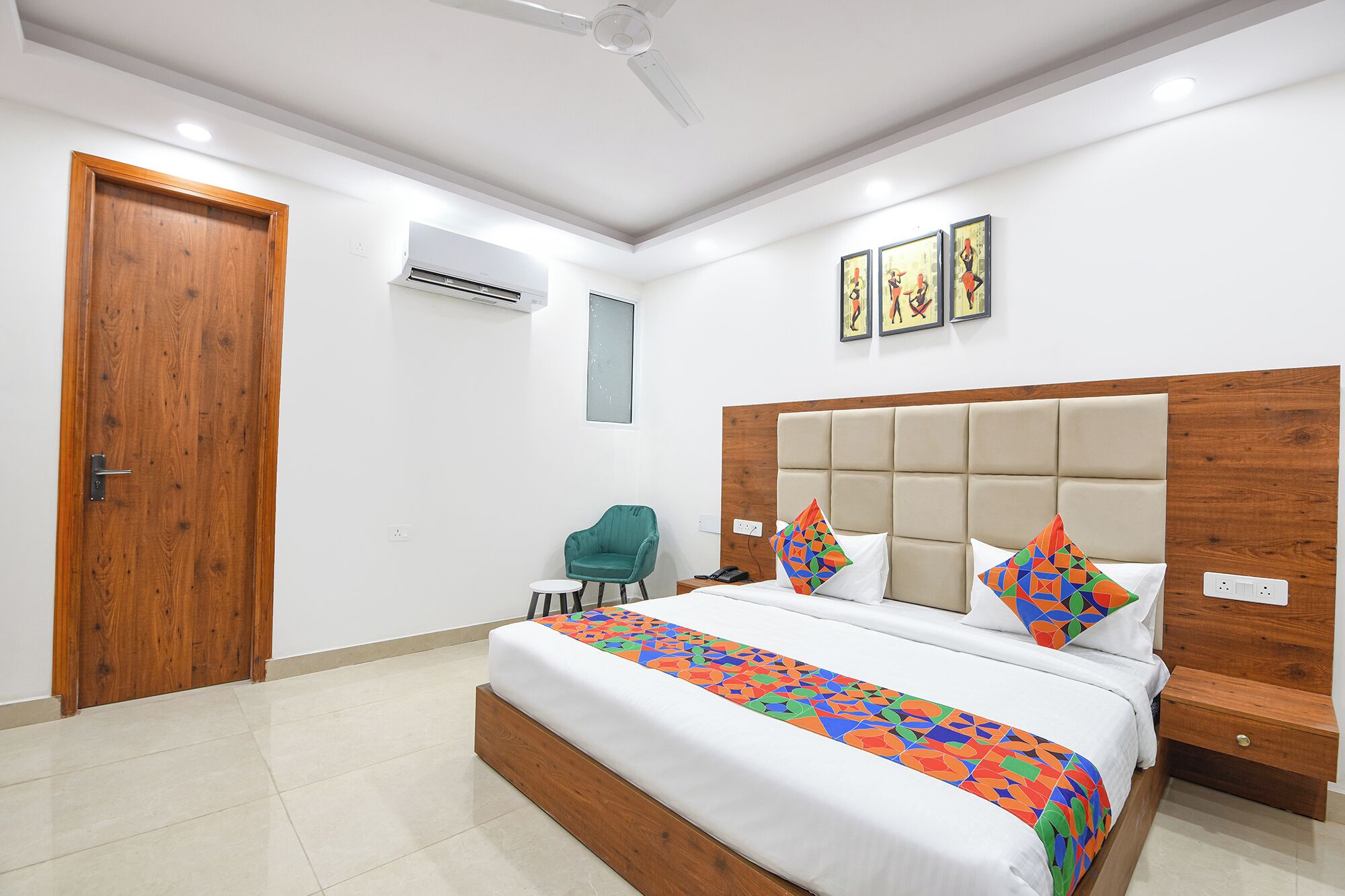 A hotel room with a large bed, a wooden headboard, a green chair, and a small table.