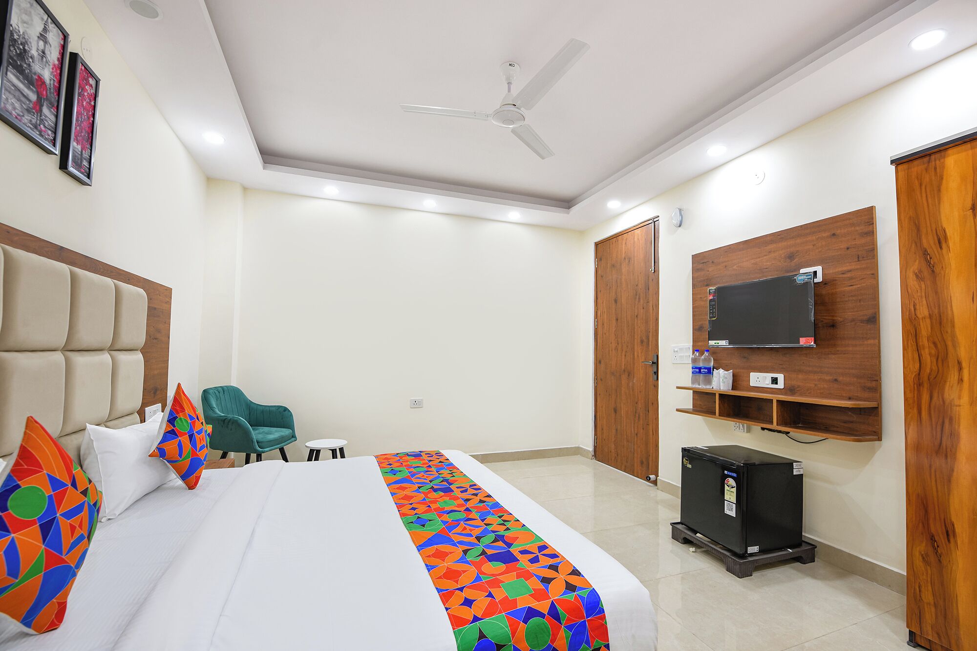 Ein Hotelzimmer mit Bett, Deckenventilator, Wand-Fernseher und einem kleinen Tisch mit Stühlen.