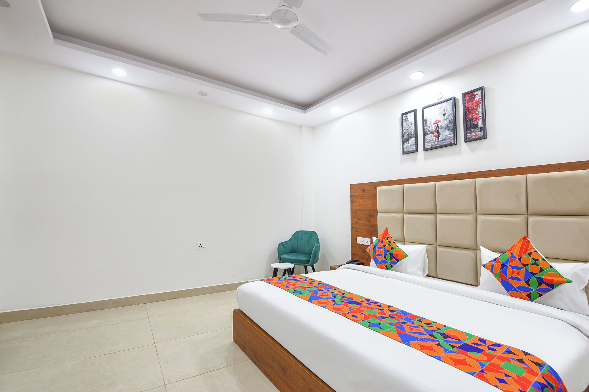 Una habitación de hotel con una cama grande, cabecera de madera y ventilador de techo. Hay tres cuadros enmarcados en la pared.