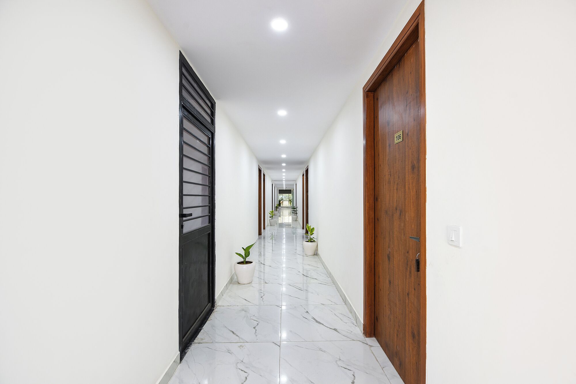 Un pasillo con paredes blancas, piso de mármol y puertas de madera.