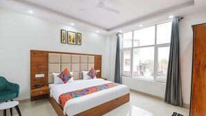 A modern hotel room with a large bed, a desk, a chair, and a window with curtains. - Fabhotel Evergreen (Faridabad)