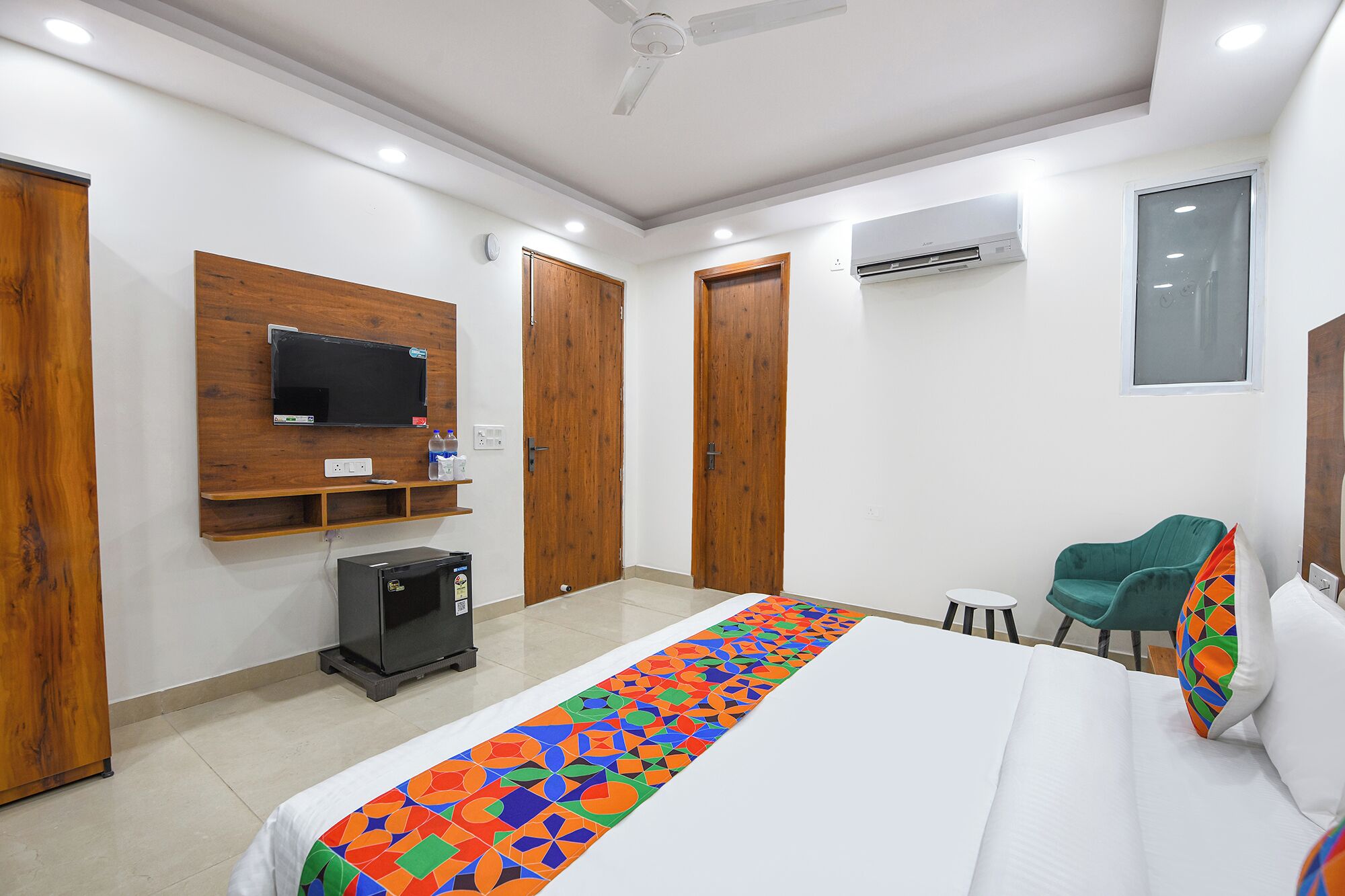 Une chambre d’hôtel avec un lit, un téléviseur fixé au mur, un réfrigérateur et une fenêtre.