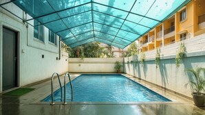 Piscina com teto de vidro, rodeada por um edifício com varandas e plantas em vasos.