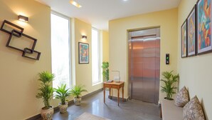 Um lobby moderno com balcão de recepção, plantas em vasos, uma obra de arte na parede e um elevador.