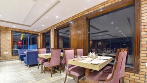 A restaurant with brick walls, large windows, and wooden tables and chairs. - Fabhotel Green Acres (Dehradun)
