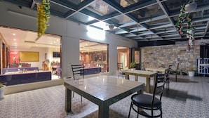 A spacious indoor area with a high ceiling, large windows, and a mix of seating arrangements including tables and chairs. - Fabhotel Green Acres (Dehradun)