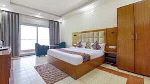 A hotel room with a large bed, a wooden wardrobe, a desk with a chair, and a view of the outside through a large window. - Fabhotel Green Acres (Dehradun)