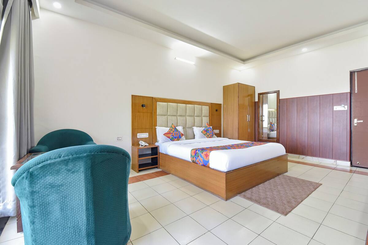 Habitació d'hotel moderna amb un llit gran, un armari de fusta, una taula de treball amb una cadira i un bany visible a través d'una porta.