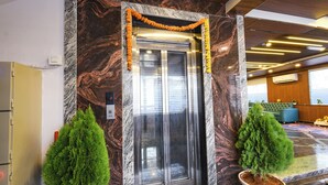 An elevator with a marble wall, two potted plants, and a garland above the door. - Fabhotel Sunrise (Hyderabad)