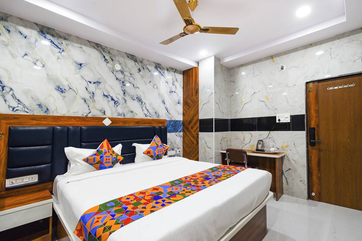 A hotel room with a bed, a nightstand, a bedside table, a ceiling fan, and marble-patterned walls.