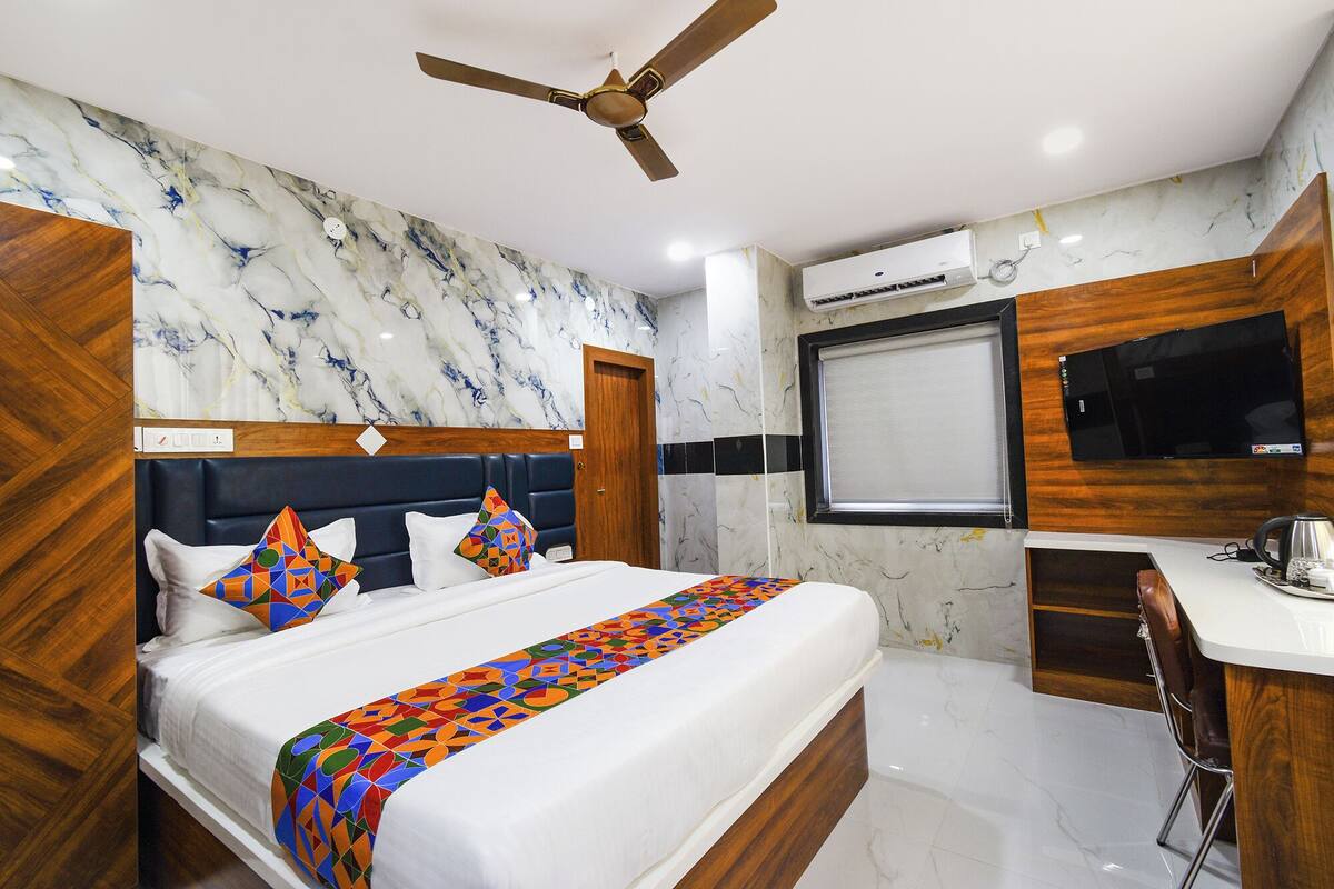 A hotel room with a bed, a ceiling fan, a TV, and an air conditioning unit.