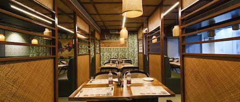 A restaurant with a long table, chairs, and hanging lights.
