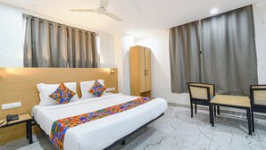 A hotel room with a bed, a desk, a chair, a wardrobe, and a ceiling fan. - FabHotel Prime Unnam (Hyderabad)