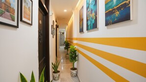 Un pasillo con cuadros enmarcados en las paredes, plantas en macetas y un diseño de rayas amarillas en la pared derecha.