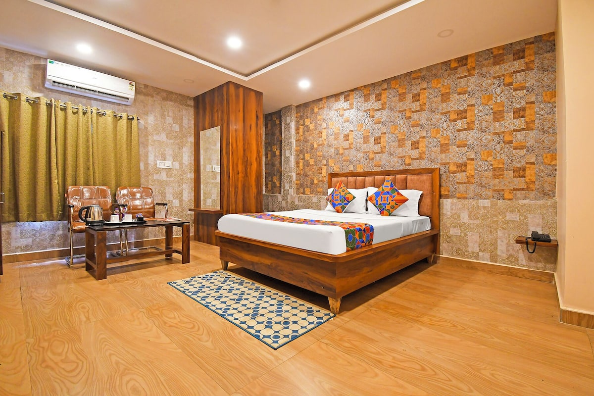 A hotel room with a wooden bed, a desk with chairs, a patterned rug, and a decorative wall.