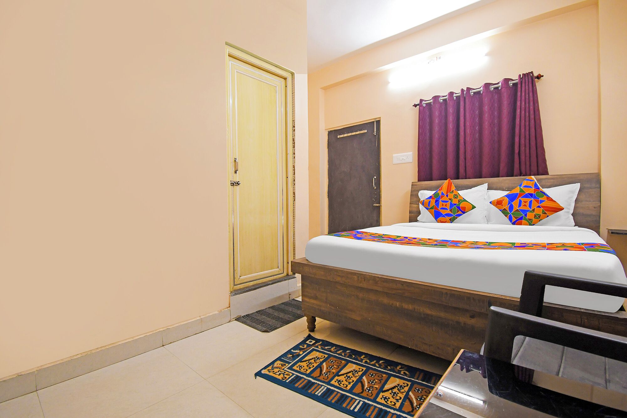 A bedroom with a wooden bed, a door, a small desk, and a patterned rug.