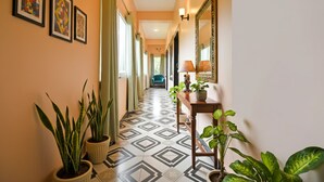 A hallway with patterned flooring, potted plants, framed artwork, and a mirror.