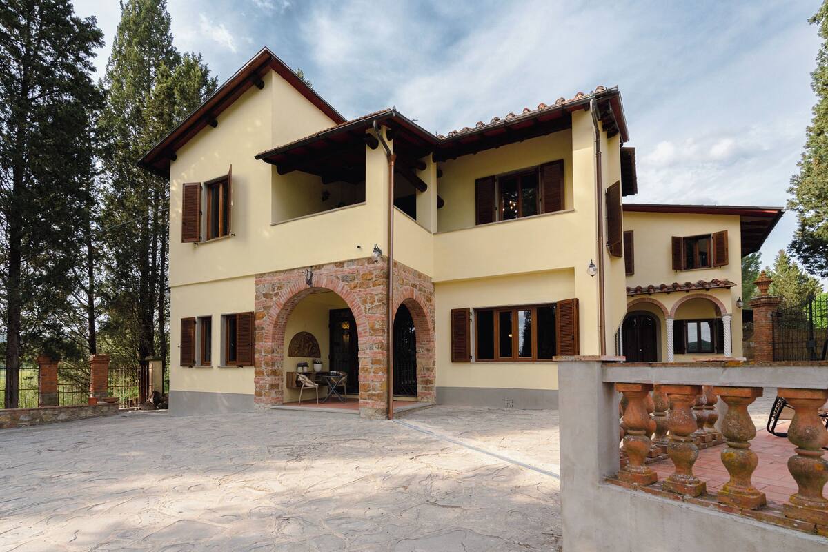 Uma casa de dois andares com fachada de pedra, várias janelas e um pátio.