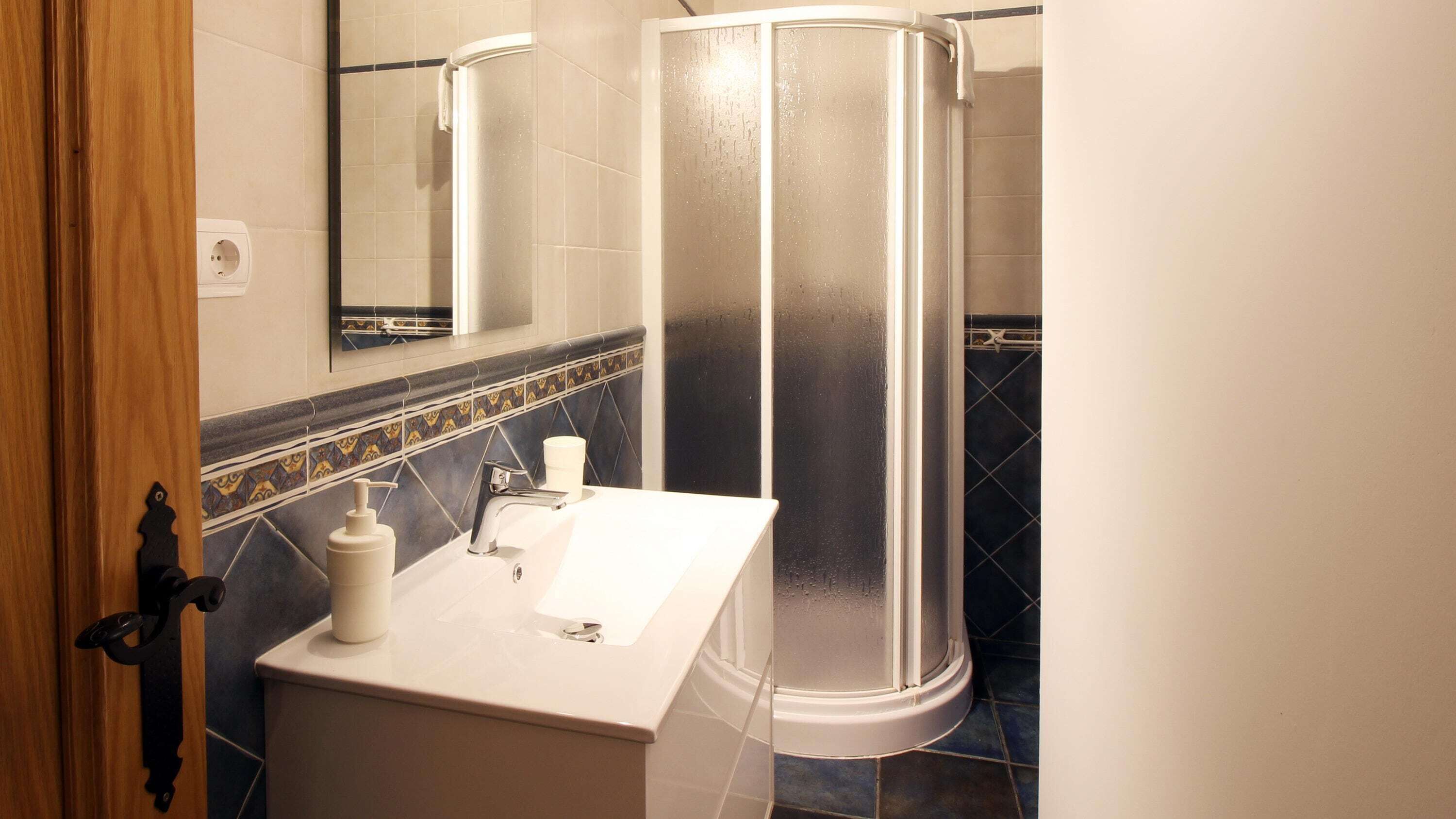 Un baño con cabina de ducha, lavamanos con espejo e inodoro.