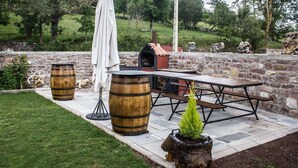 Une terrasse extérieure avec un mur en pierre, une table en bois, des bancs et un barbecue.