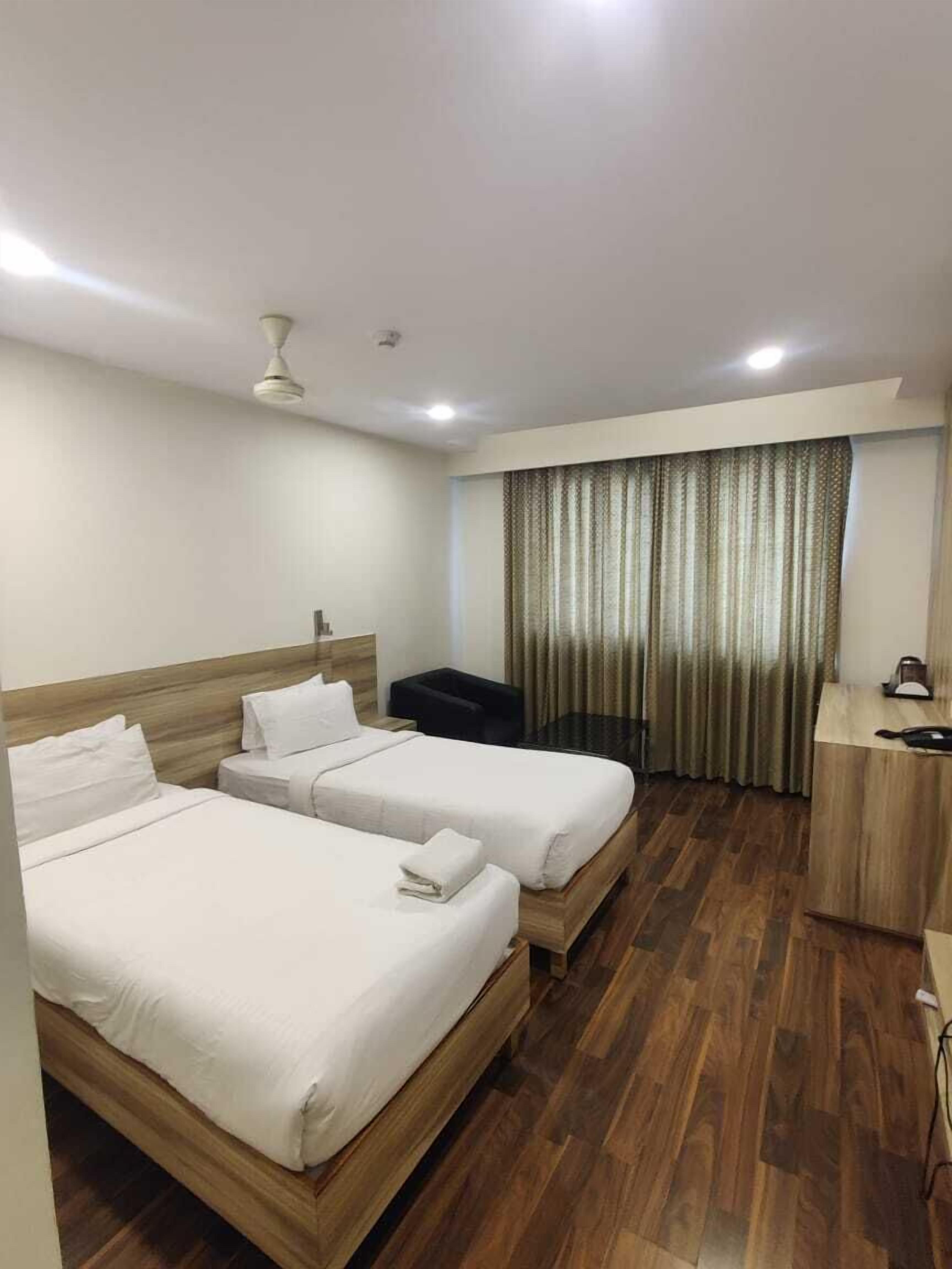 Una habitación de hotel con dos camas, un escritorio, una silla y una cortina.