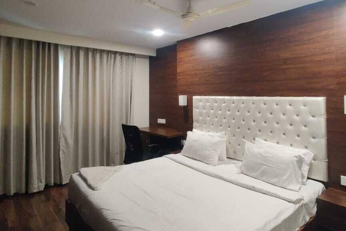 Ein Hotelzimmer mit einem großen Bett, einem Schreibtisch, einem Stuhl, einem Deckenventilator und einem Fenster mit Vorhängen.