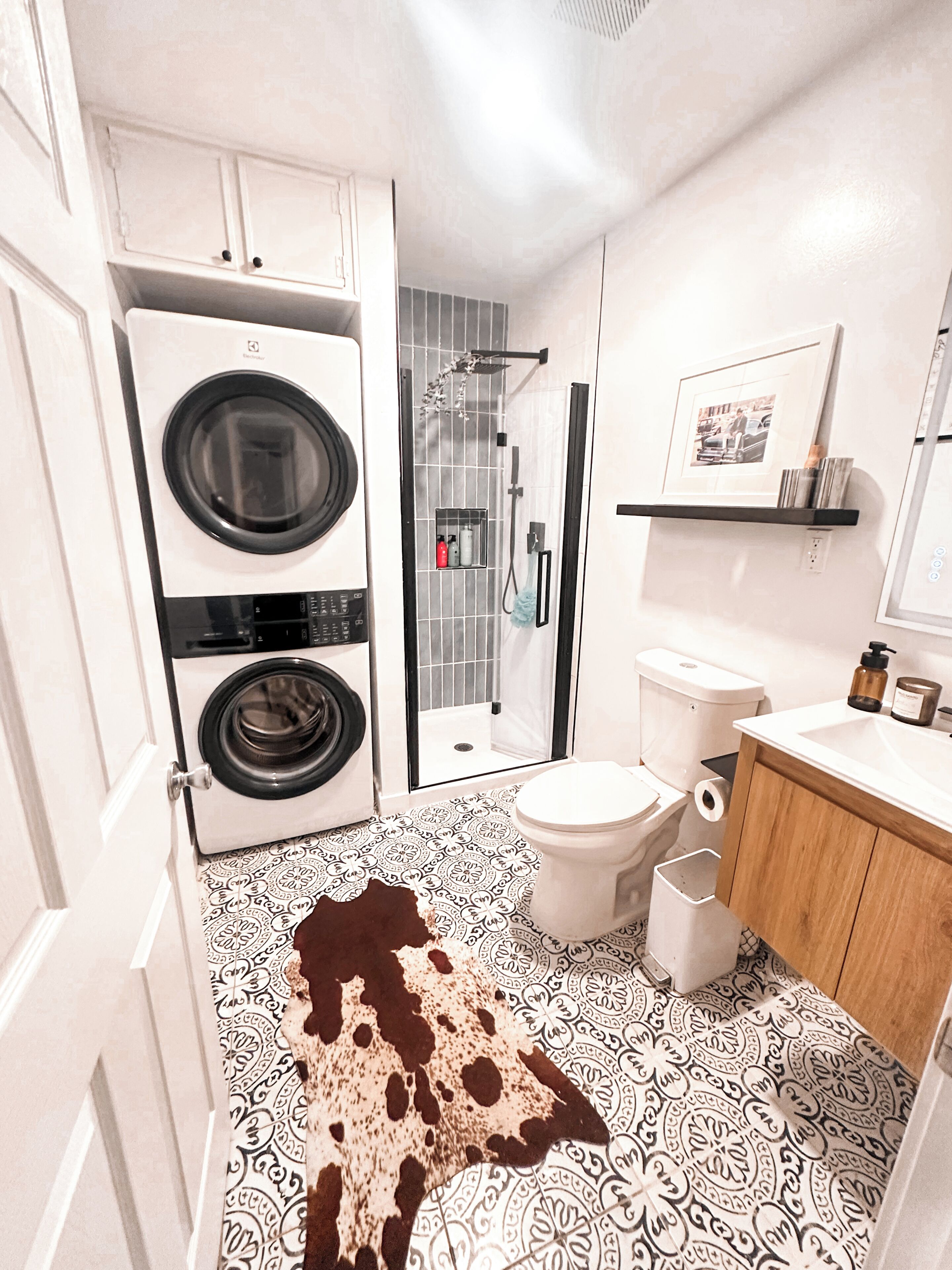 A modern bathroom with a washing machine, toilet, shower, and sink.