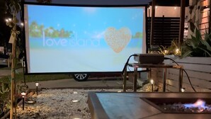 Zona de estar al aire libre con una pantalla grande que muestra 'loveislana' y un símbolo de corazón.