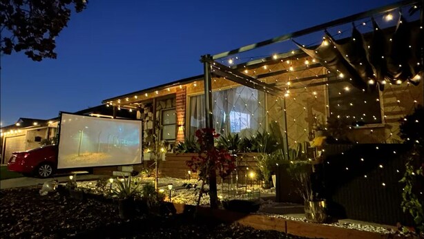 Una casa con una pantalla grande mostrando una imagen, rodeada de luces y plantas exteriores.