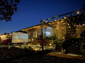 A house with a large screen displaying an image, surrounded by outdoor lights and plants. - Charming family home in quiet and cozy Lakewood. (Lakewood)