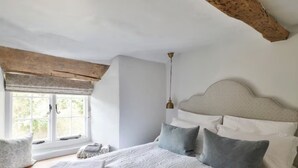 A bedroom with a large bed, a window with a view, and a wooden ceiling beam.