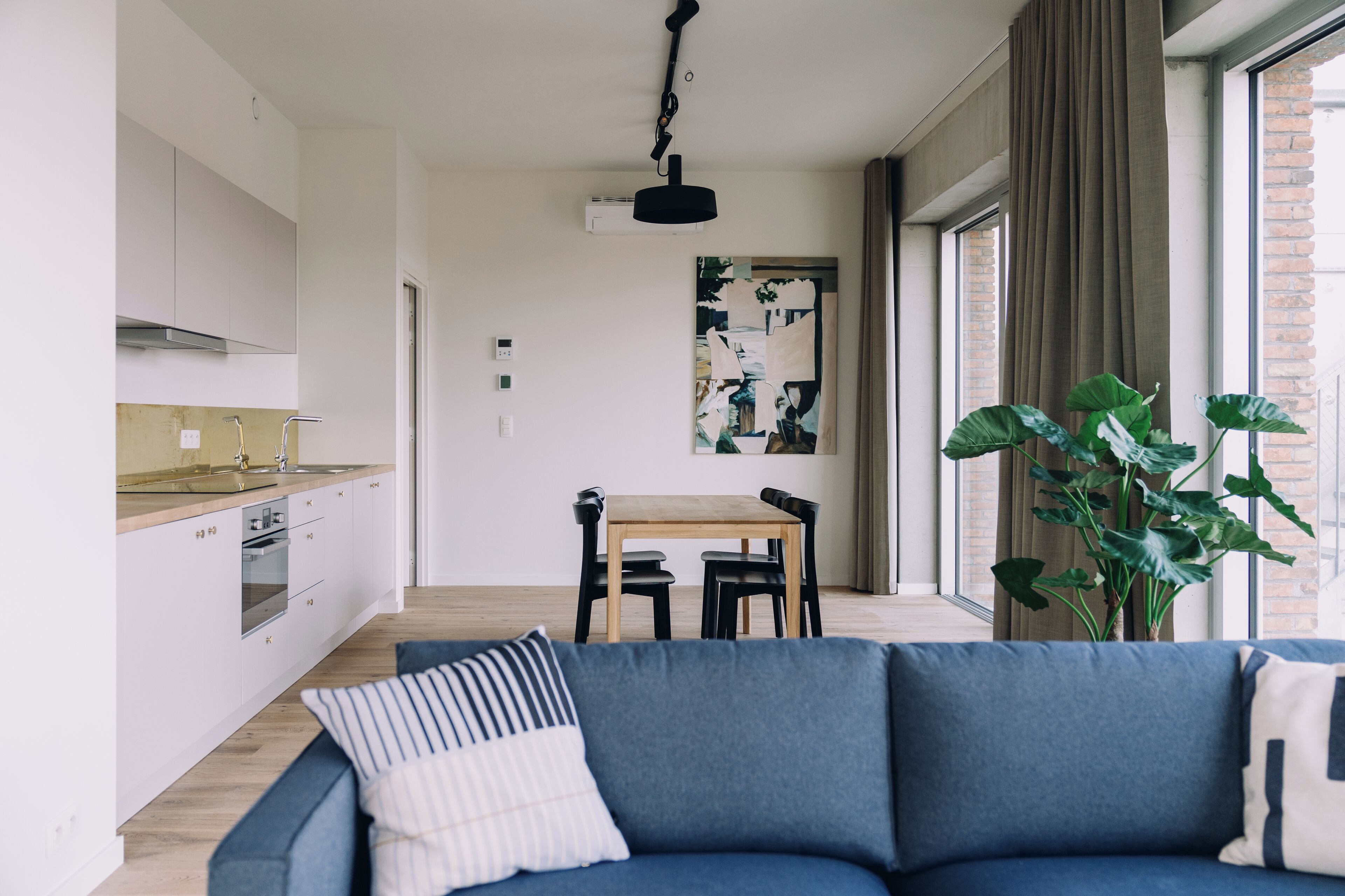 A modern kitchen with white cabinets, a wooden dining table, and a blue sofa with striped pillows.